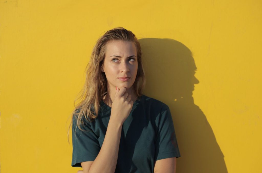 pexels photo 3858017 3858017 A thoughtful woman poses against a vibrant yellow wall, casting a shadow.